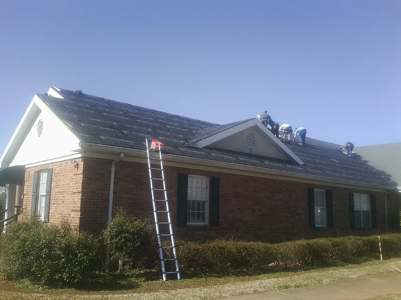 Crew tearing shingles off a brick ranch roof with a ladder set — Emergency Roof Repair work by our crew in Waldo