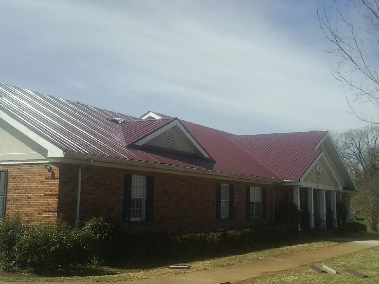 Red metal roof with gabled entries on a long brick building, from a Hail Damage Roof Repair job in Waldo