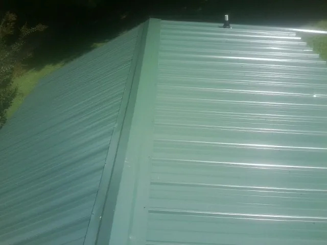 New green metal panels meeting at the ridge of a roof — Flat Roof Repair work by our crew in Waldo